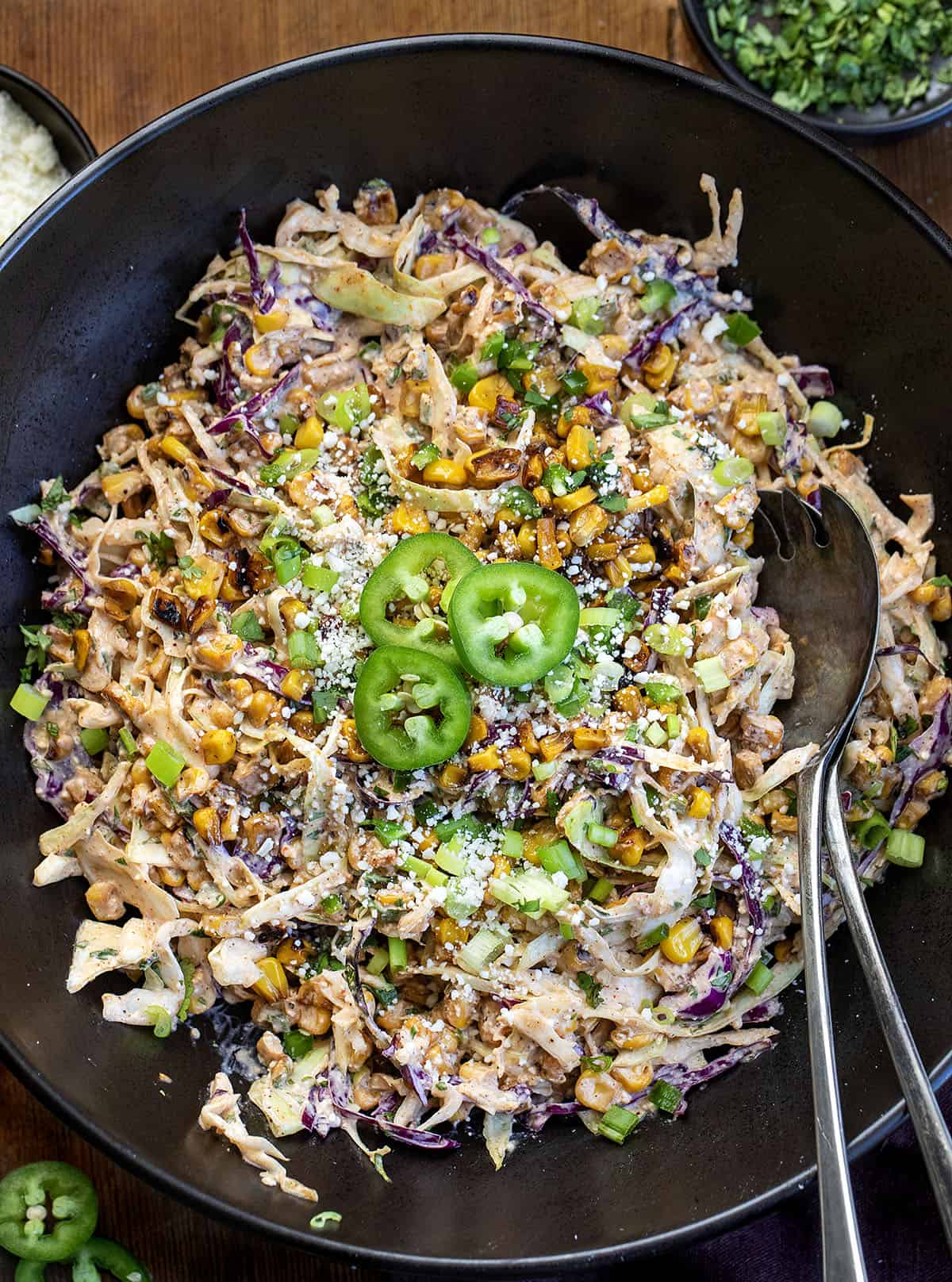 This Mexican Street Corn Slaw is a fresh, crunchy side dish inspired by classic elote. It’s made with shredded cabbage, sweet corn, a creamy lime dressing, and just the right amount of spice! Close up of a bowl of Mexican Street Corn Slaw with serving spoons in it.