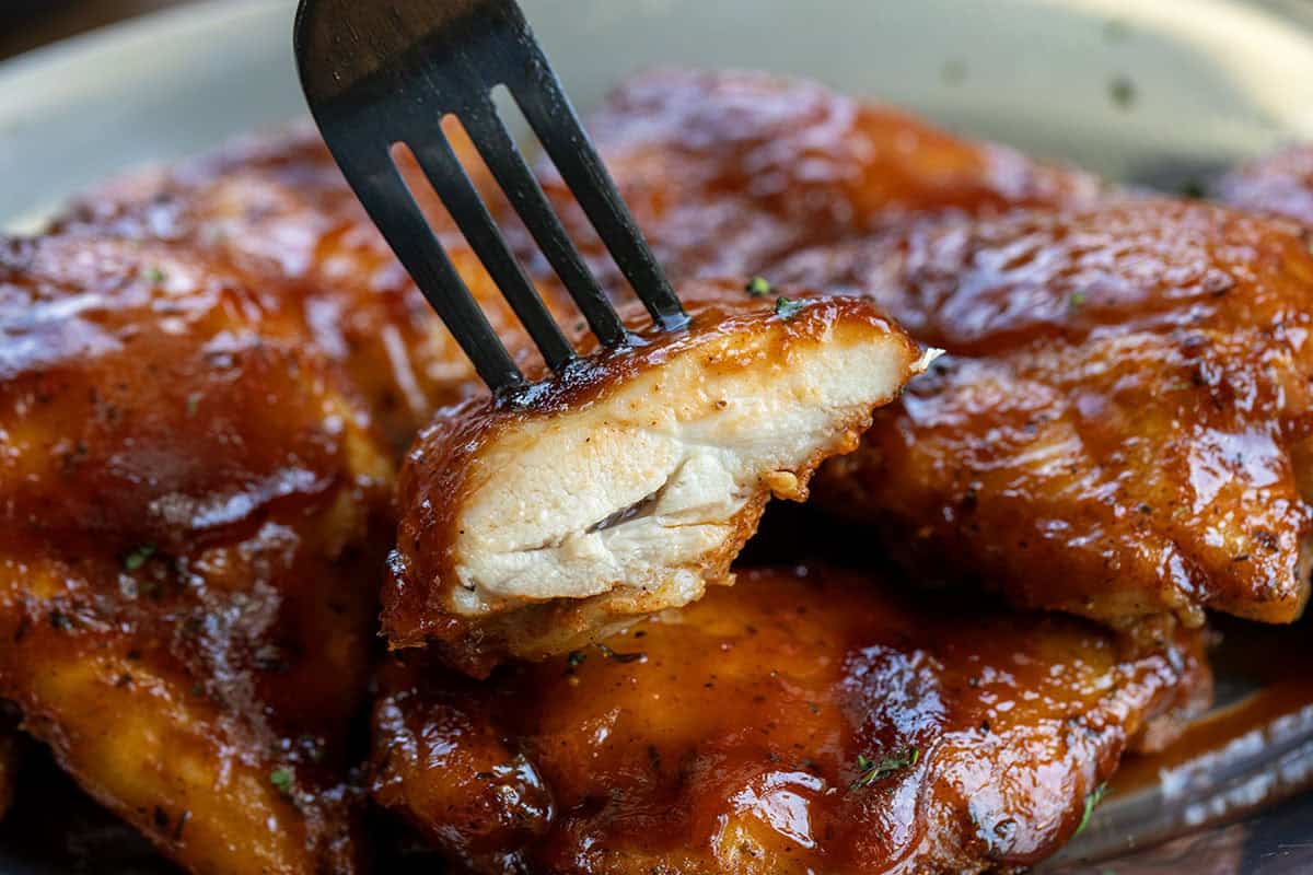 One cut piece of Oven Baked BBQ Chicken Thigh held up with a fork over the chicken.