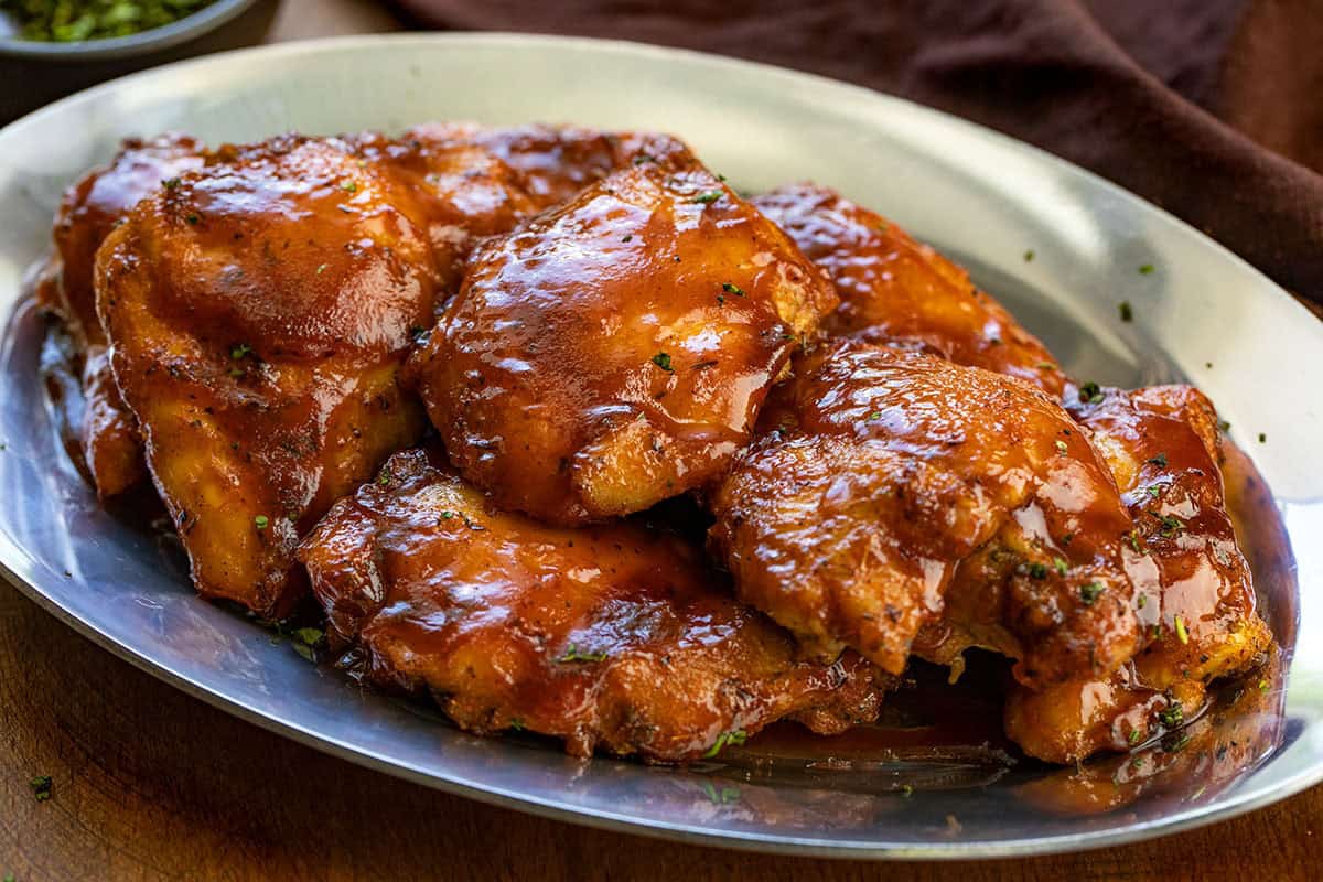 Oven Baked BBQ Chicken Thighs on a metal platter on a wooden table.