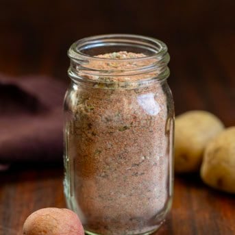 Jar of Potato Seasoning on a wooden table with small potatoes.