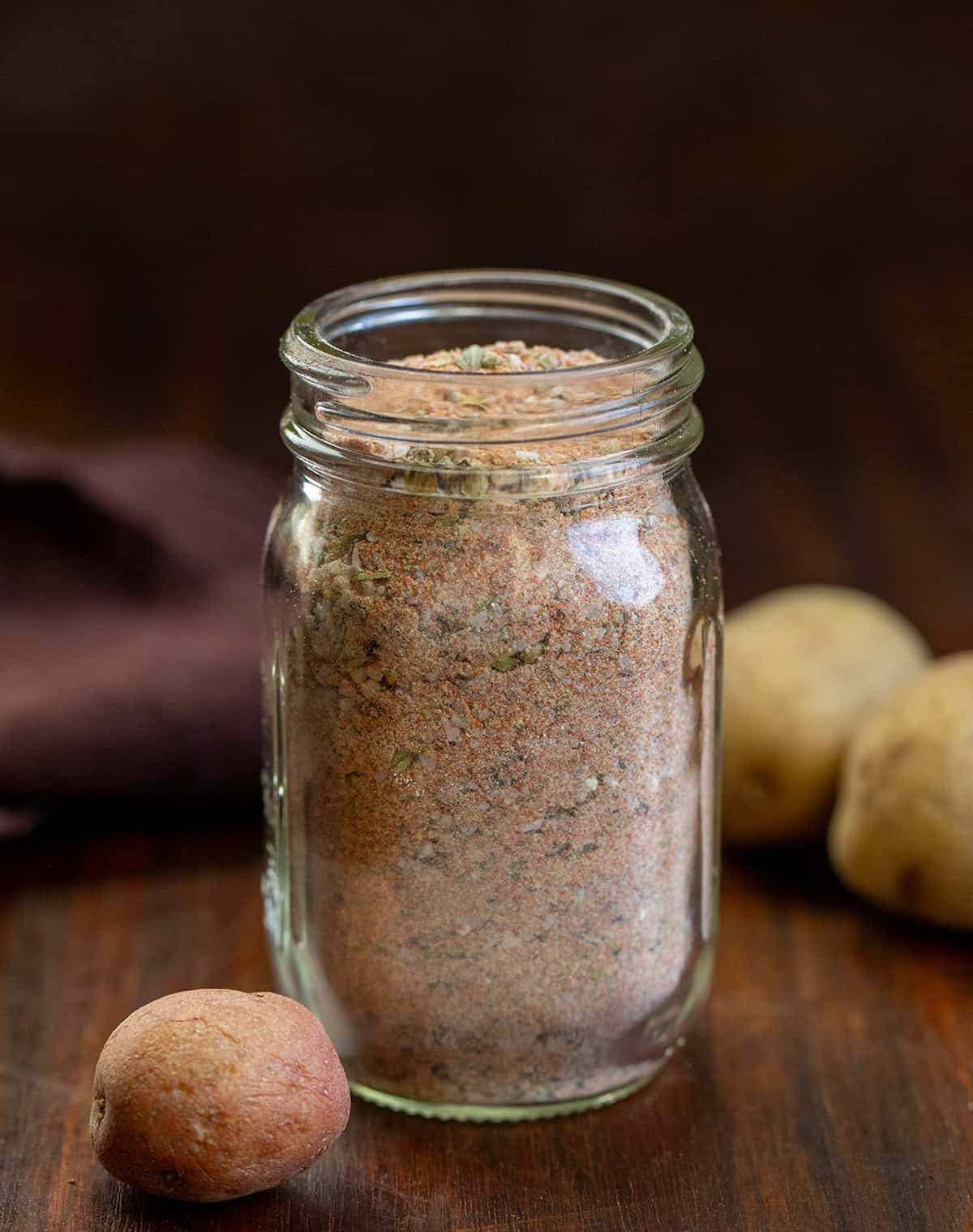 This homemade Potato Seasoning is a simple, savory blend that takes roasted, baked, or air-fried potatoes to the next level! Jar of Potato Seasoning on a wooden table with small potatoes.