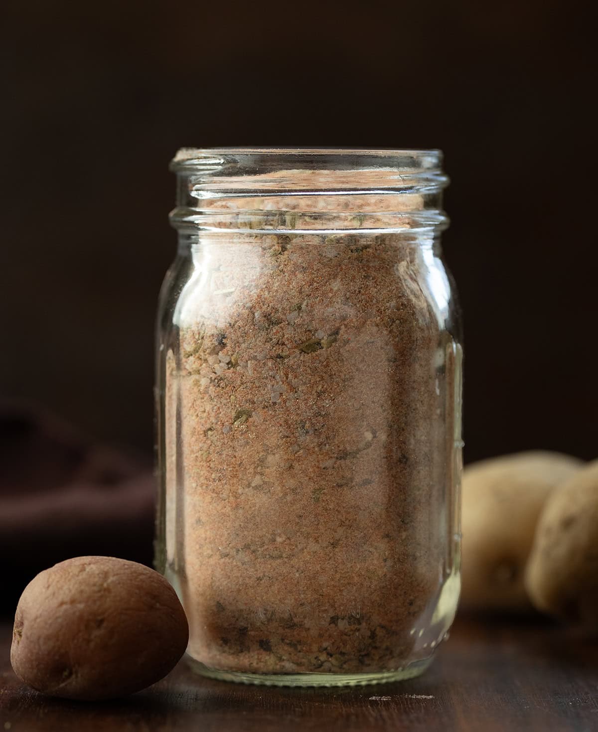 This homemade Potato Seasoning is a simple, savory blend that takes roasted, baked, or air-fried potatoes to the next level! Jar of Potato Seasoning on a wooden table with small potatoes.