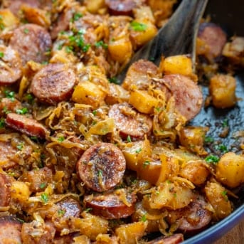 Close up in the skillet of Skillet Kielbasa and Sauerkraut with a wooden spoon.