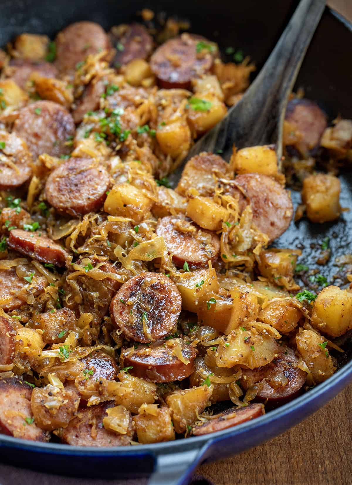Close up in the skillet of Kielbasa and Sauerkraut with a wooden spoon Close up in the skillet of Kielbasa and Sauerkraut with a wooden spoon.