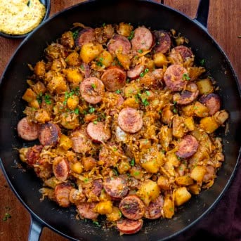 Looking down into a skillet of Skillet Kielbasa and Sauerkraut on a wooden table.