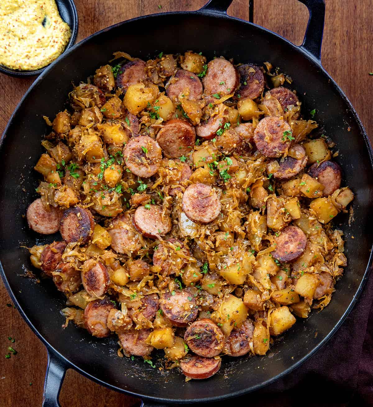 skillet of Kielbasa and Sauerkraut on a wooden table Looking down into a skillet of Kielbasa and Sauerkraut on a wooden table.