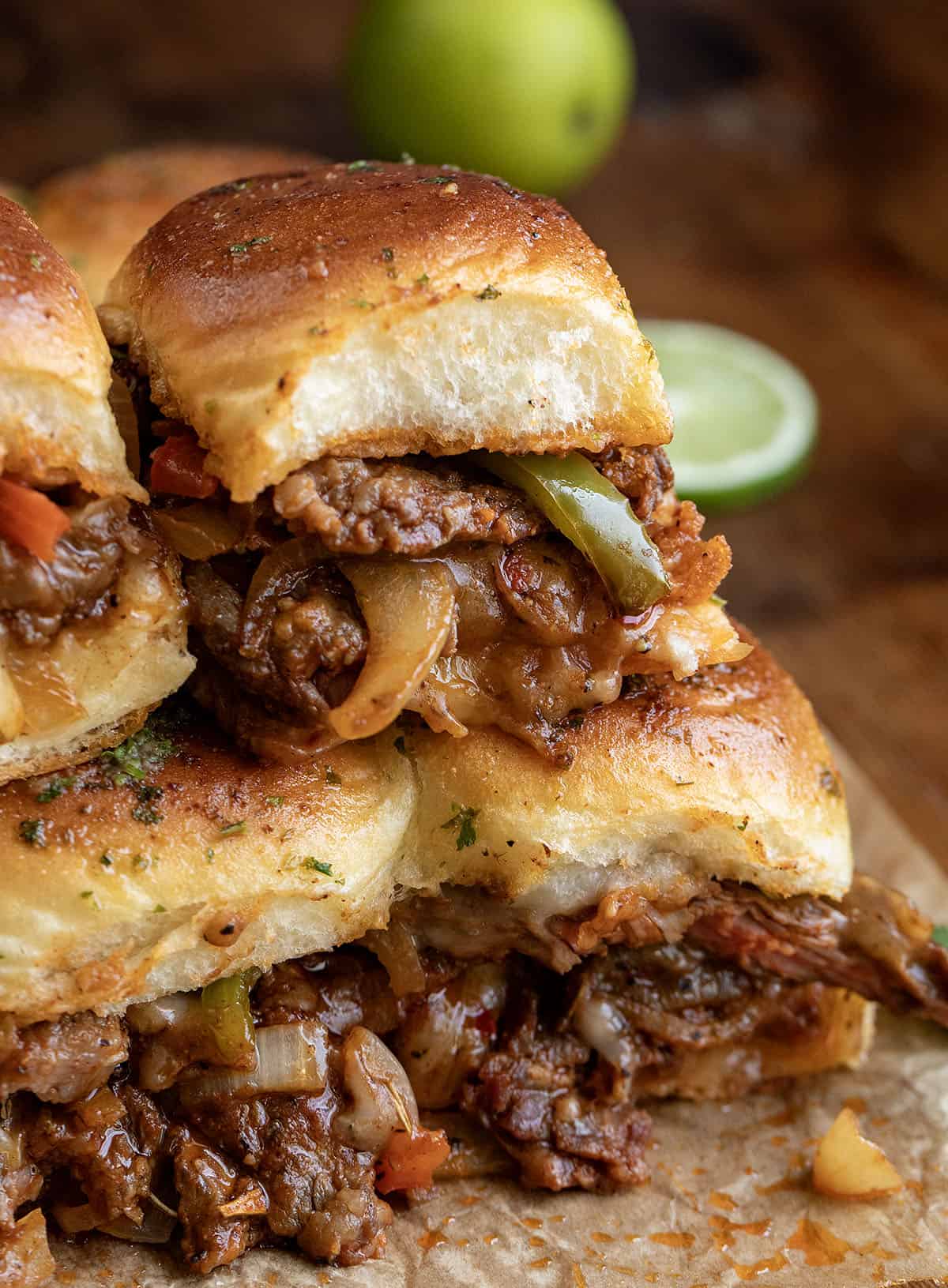These Steak Fajita Sliders are loaded with tender, seasoned steak, sautéed peppers and onions, and melty cheese all baked inside soft Hawaiian rolls! Stacked Steak Fajita Sliders on a wooden table.