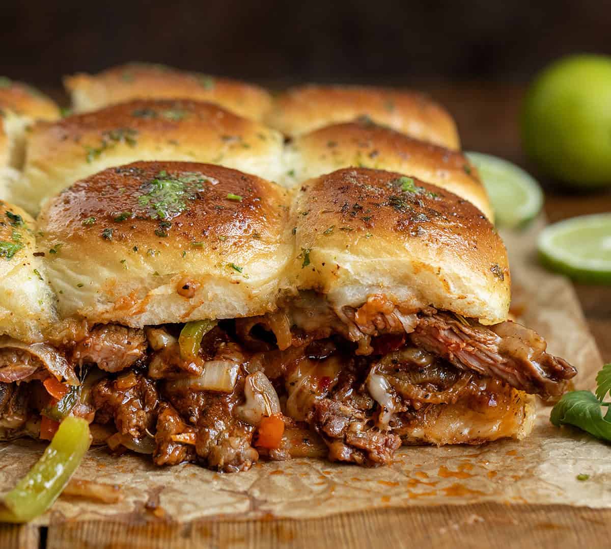 These Steak Fajita Sliders are loaded with tender, seasoned steak, sautéed peppers and onions, and melty cheese all baked inside soft Hawaiian rolls! Close up of Steak Fajita Sliders showing juicy steak and fresh limes.