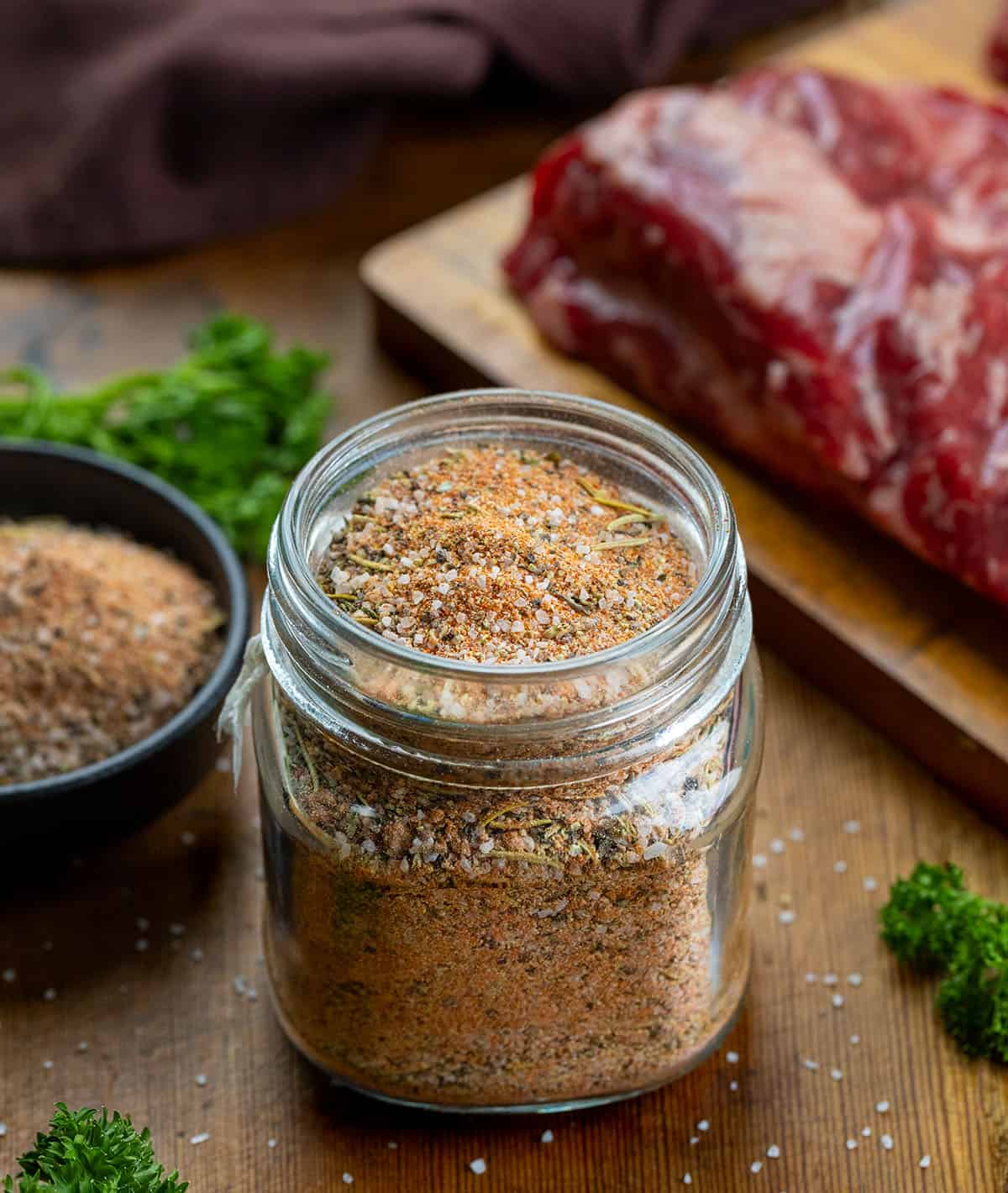 This homemade steak seasoning is bold, savory, and packed with classic steakhouse flavor in every pinch. Keep a jar on hand and you’ll never need store-bought seasoning again! Glass jar of Steak Seasoning on a wooden table next to a steak.