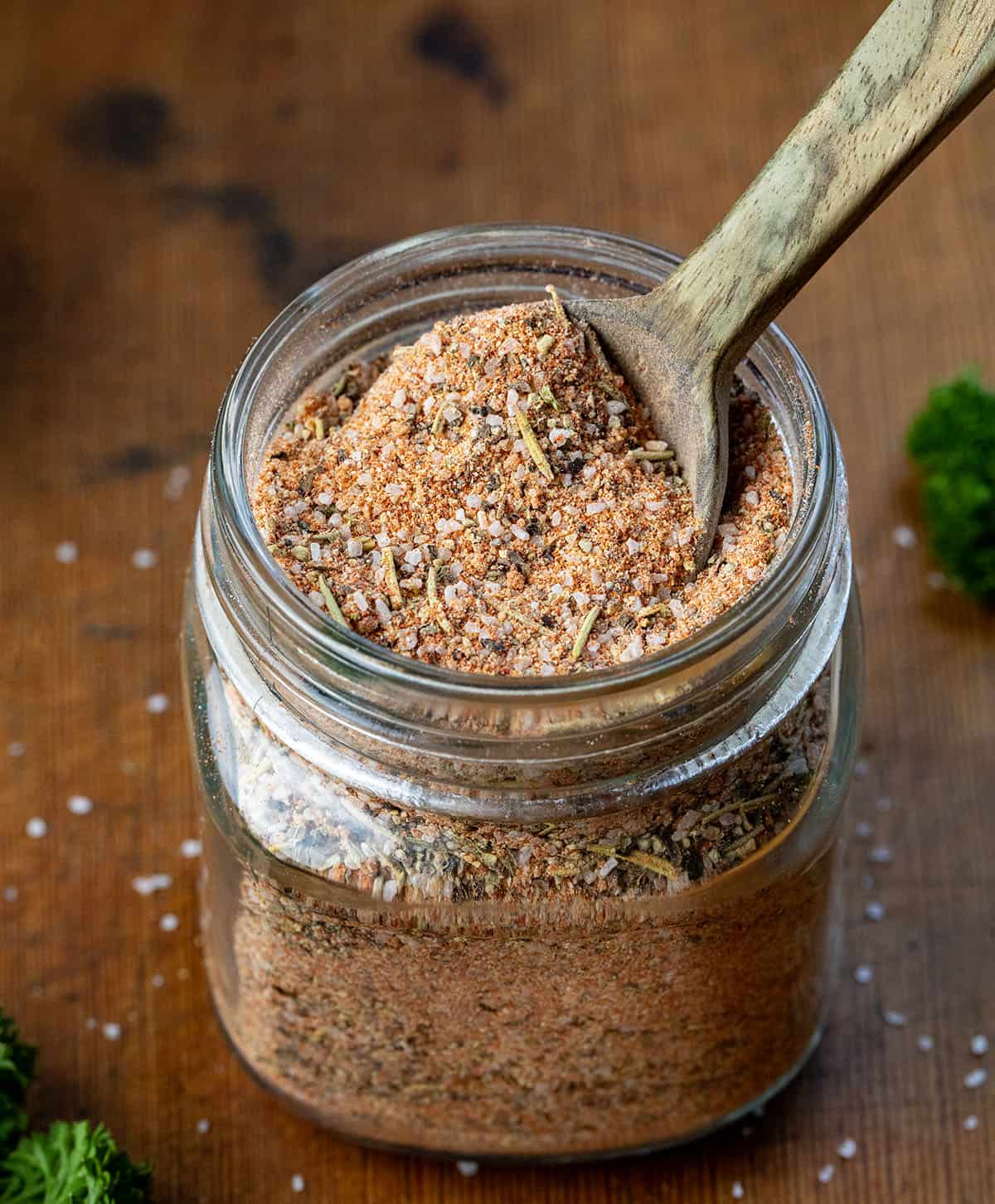 This homemade steak seasoning is bold, savory, and packed with classic steakhouse flavor in every pinch. Keep a jar on hand and you’ll never need store-bought seasoning again! Close up of a jar of Steak Seasoning with a wooden measuring spoon in it on a wooden table.