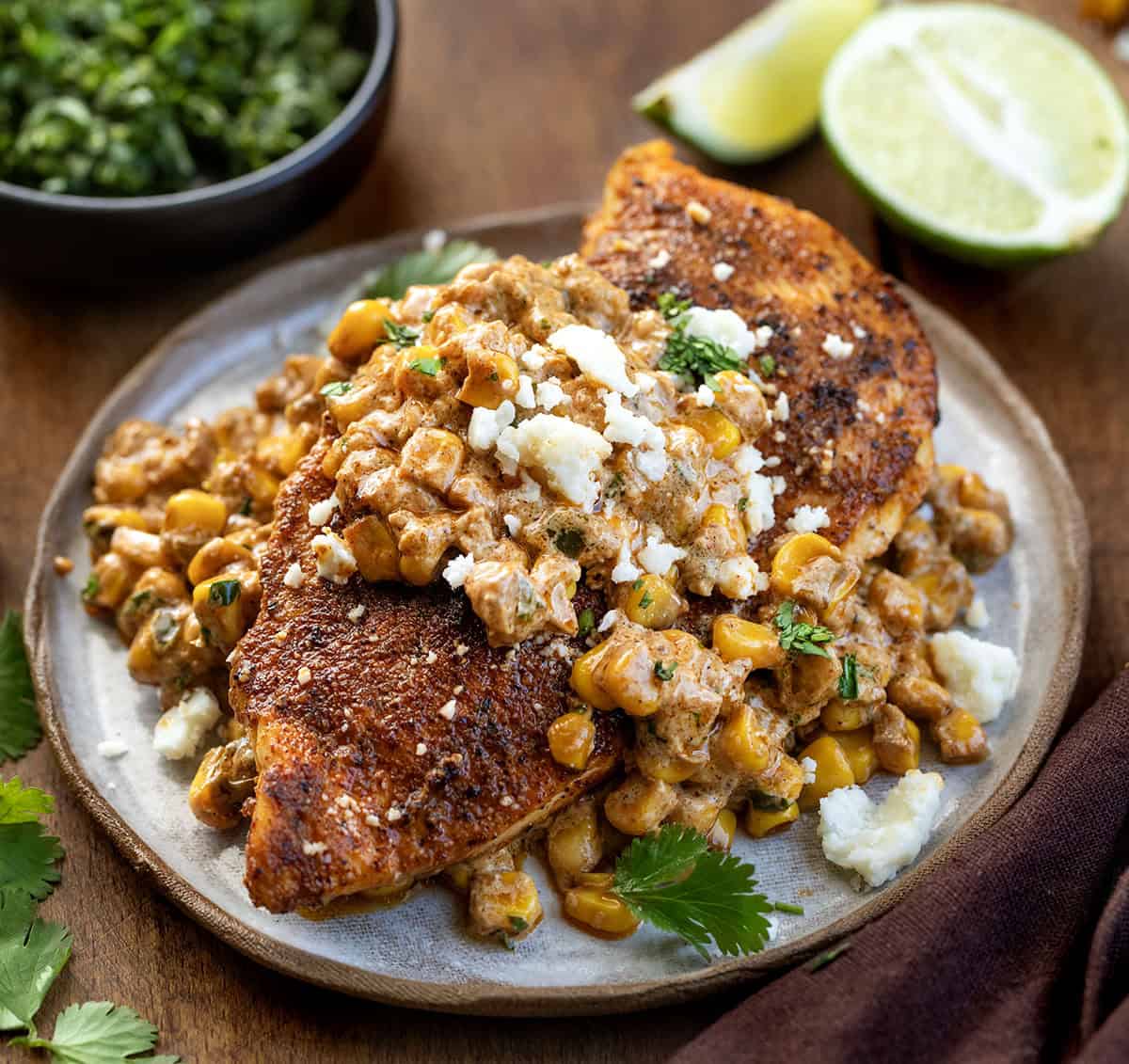 If you love Mexican street corn (elote), you are going to flip for this Creamy Street Corn Chicken Skillet! Juicy seasoned chicken is smothered in a rich, cheesy corn sauce with lime, Cotija, and just the right kick Plate with Street Corn Chicken Skillet on it covered in the corn sauce.