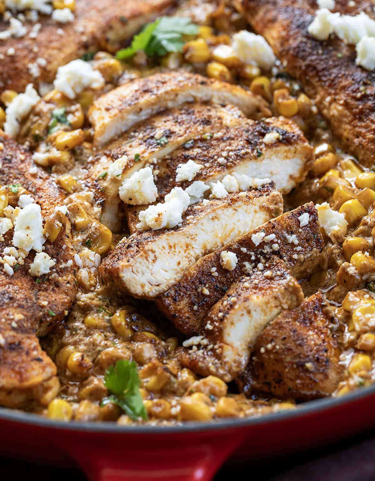 If you love Mexican street corn (elote), you are going to flip for this Creamy Street Corn Chicken Skillet! Juicy seasoned chicken is smothered in a rich, cheesy corn sauce with lime, Cotija, and just the right kick Close up of sliced Street Corn Chicken in a skillet.
