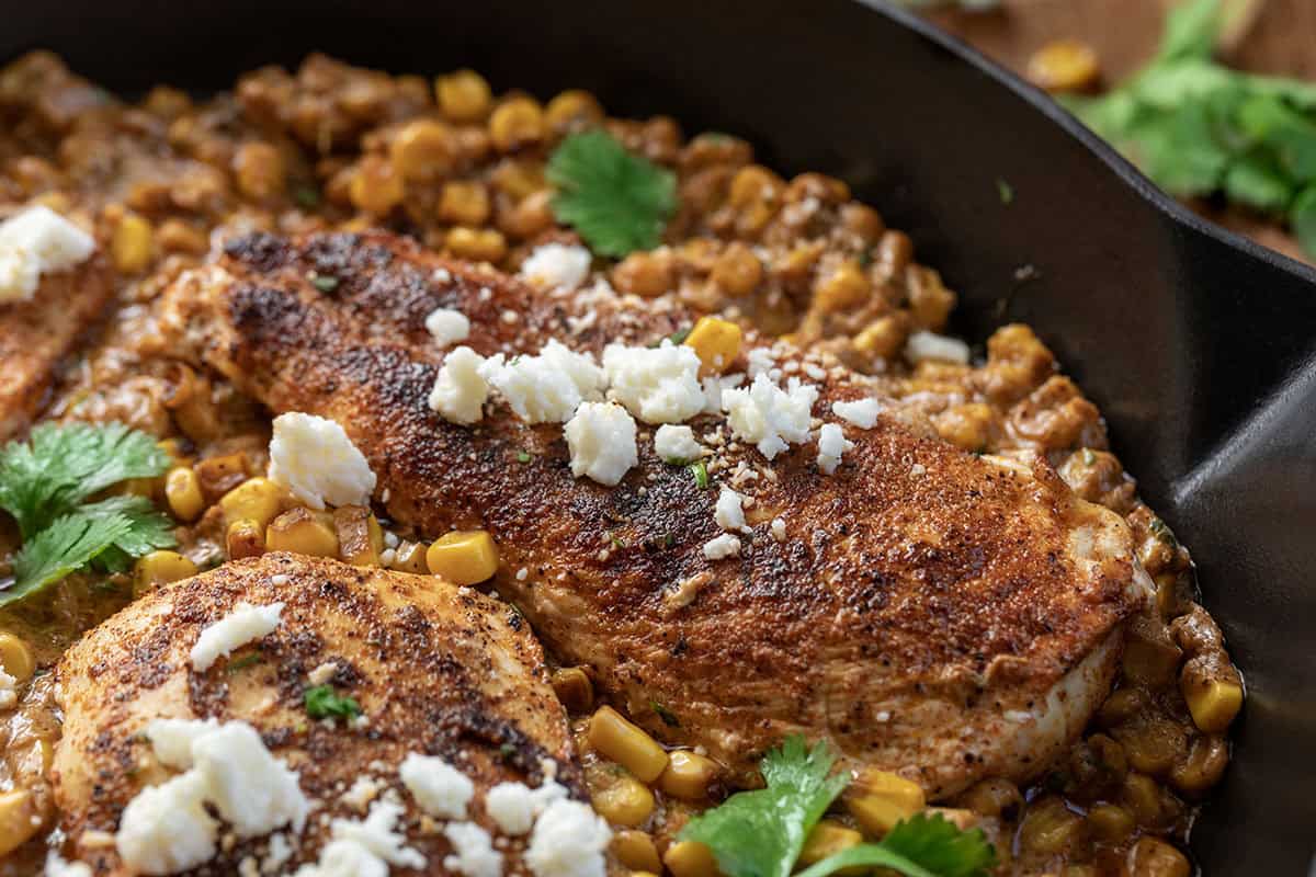 If you love Mexican street corn (elote), you are going to flip for this Creamy Street Corn Chicken Skillet! Juicy seasoned chicken is smothered in a rich, cheesy corn sauce with lime, Cotija, and just the right kick Close up of Street Corn Chicken Skillet in a skillet showing tender, moist chicken.