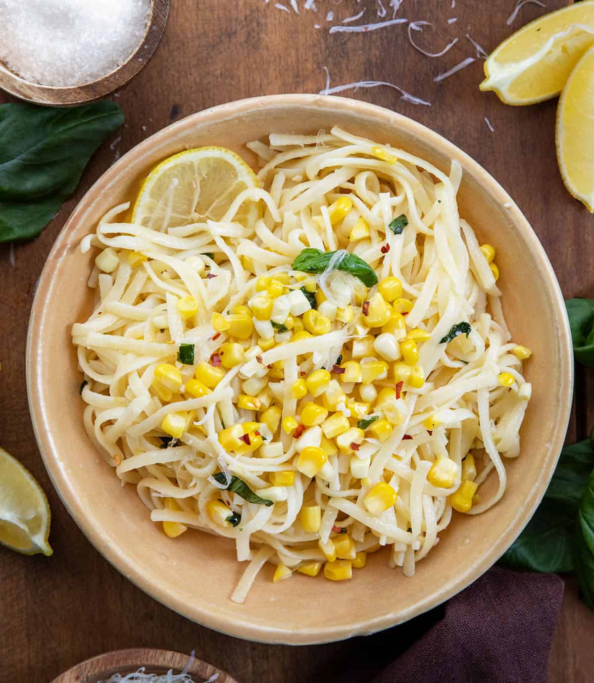 Bowl of Summer Lemon Corn Pasta on a wooden table with fresh lemon and basil Bowl of Summer Lemon Corn Pasta on a wooden table with fresh lemon and basil.