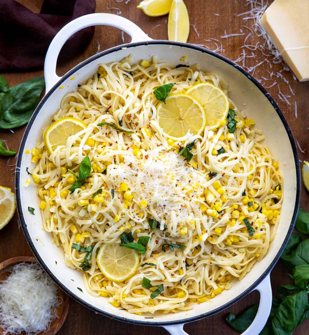 Skillet of Summer Lemon Corn Pasta on a wooden table from overhead surrounded by fresh parmesan, lemon, and basil Skillet of Summer Lemon Corn Pasta on a wooden table from overhead surrounded by fresh parmesan, lemon, and basil.