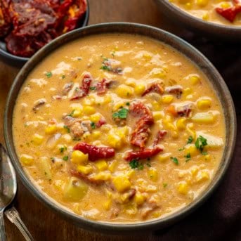 Bowls of Sun-Dried Tomato Corn Chowder on a wooden table with sun-dried tomatoes.