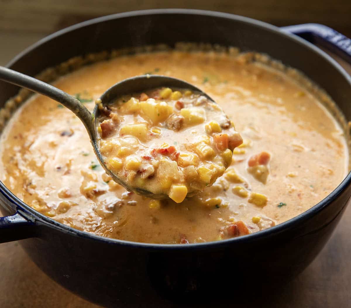 This Sun-Dried Tomato Corn Chowder is a rich, creamy soup made with sweet corn, tender vegetables, smoky bacon, and sun-dried tomatoes for extra depth of flavor! Ladle picking up a scoop of Sun-Dried Tomato Corn Chowder from the pot.