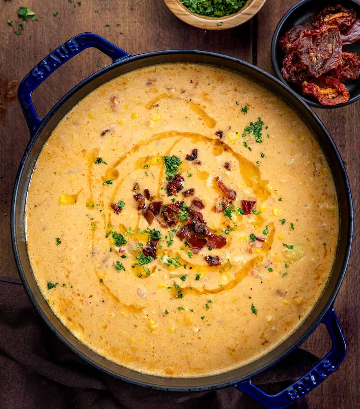 This Sun-Dried Tomato Corn Chowder is a rich, creamy soup made with sweet corn, tender vegetables, smoky bacon, and sun-dried tomatoes for extra depth of flavor! Pot of Sun-Dried Tomato Corn Chowder on a wooden table from overhead.