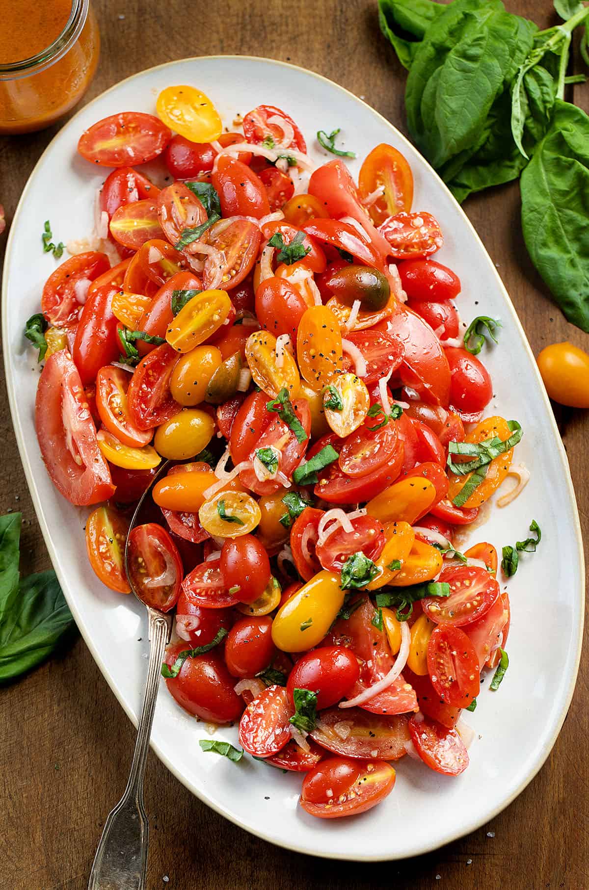 This Simple Tomato Salad is one of the easiest ways to use up ripe, juicy tomatoes when they’re at their peak. Whether they’re coming straight from the garden or picked up at the farmers’ market, this is the kind of recipe that lets the tomatoes do most of the work, and I absolutely love it! Platter of Tomato Salad on a wooden table with fresh tomatoes and basil around the dish.