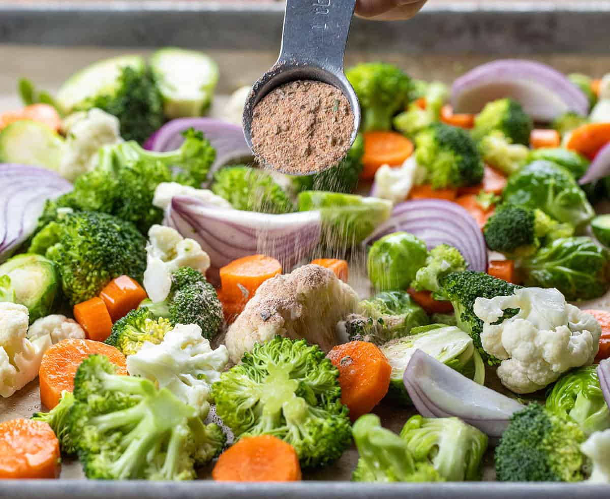 Make your own Vegetable Seasoning blend in 5 minutes! This savory homemade mix with garlic, onion, paprika & herbs elevates roasted broccoli, potatoes, carrots & more. Better than store-bought! Sprinkling Vegetable Seasoning over a sheet pan covered in fresh vegetables.