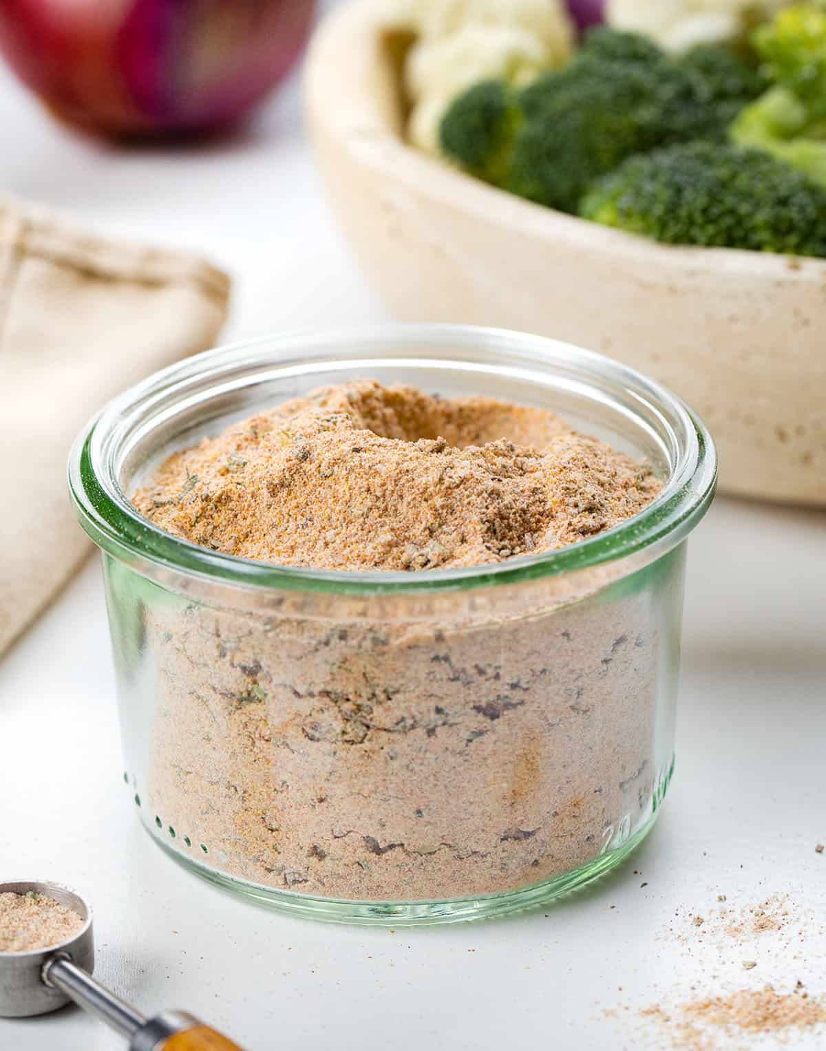 Make your own Vegetable Seasoning blend in 5 minutes! This savory homemade mix with garlic, onion, paprika & herbs elevates roasted broccoli, potatoes, carrots & more. Better than store-bought! Glass jar of Vegetable Seasoning near a bowl of vegetables.