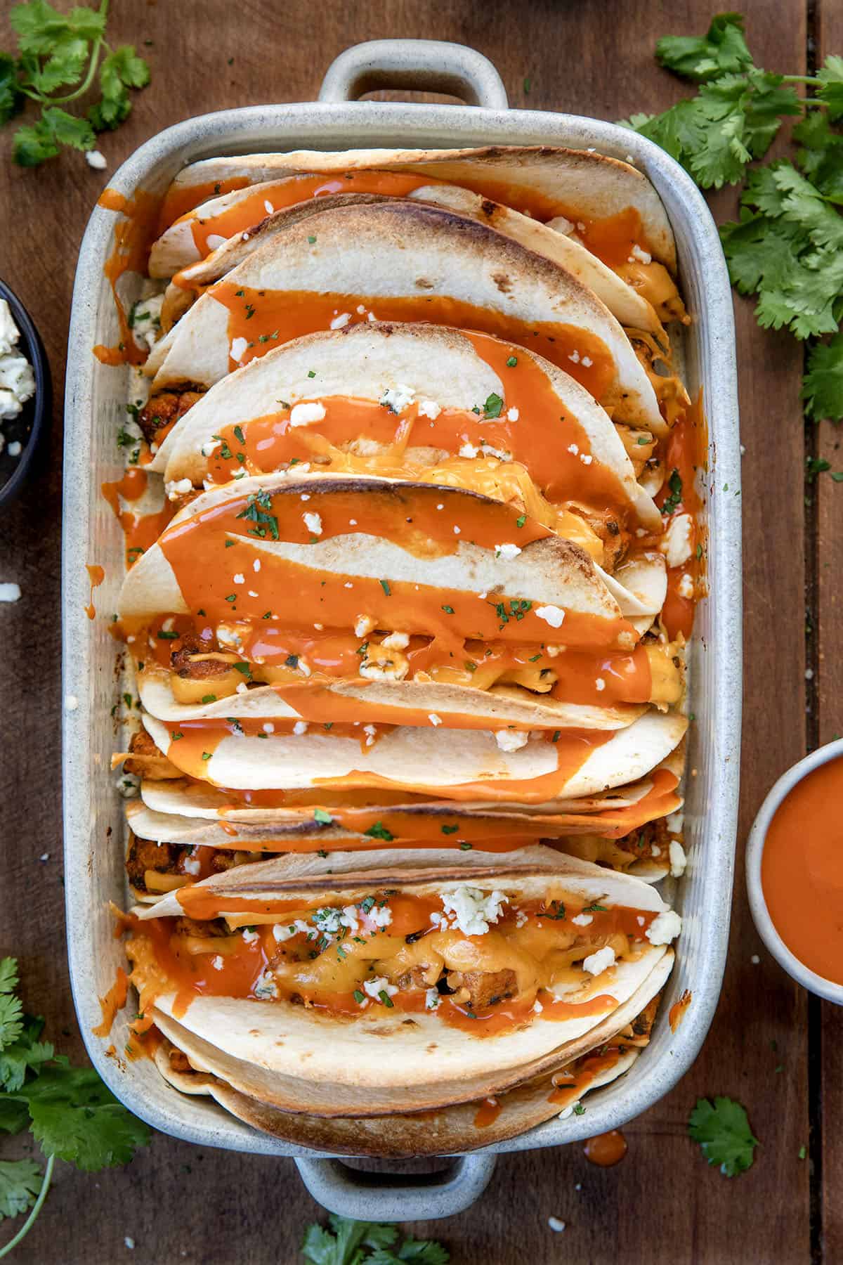 Baked Buffalo Chicken Tacos in a baking dish on a wooden table Baked Buffalo Chicken Tacos in a baking dish on a wooden table.