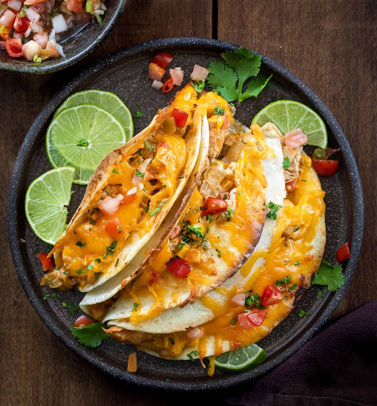 Black plate with 3 Baked Chicken Tacos on it on a wooden table from overhead.