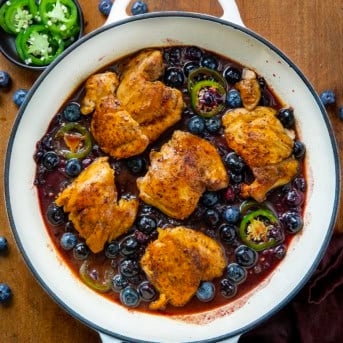 White skillet of Blueberry Jalapeño Chicken on a wooden table with fresh jalapeno and blueberries