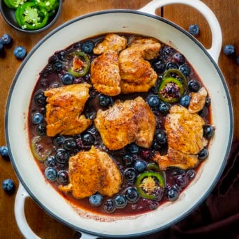 White skillet of Blueberry Jalapeño Chicken on a wooden table with fresh jalapeno and blueberries.