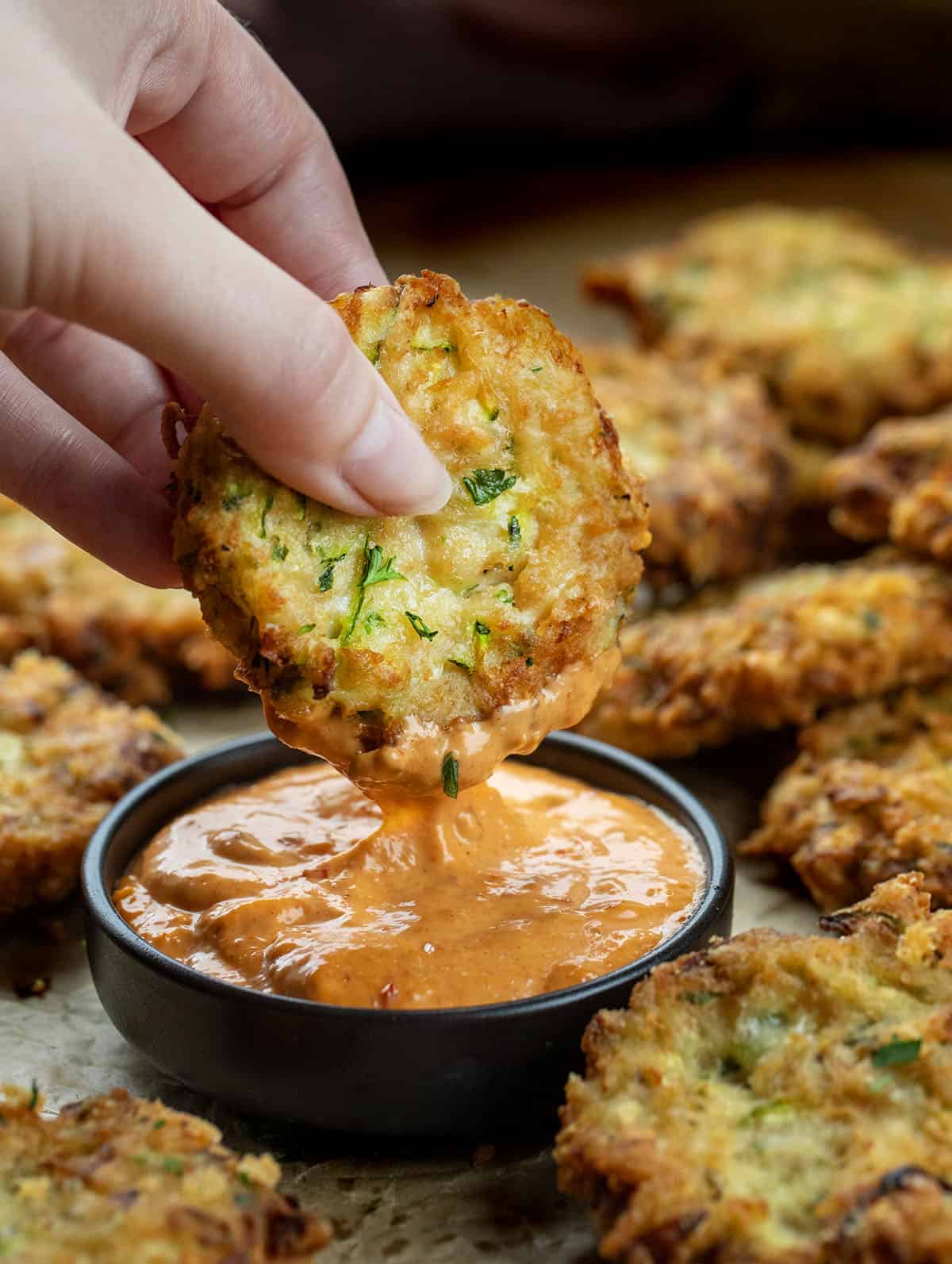 Hand holding a Cheesy Zucchini Chicken Fritter in dipping sauce.