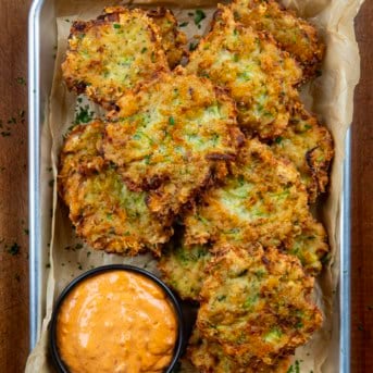 Cheesy Zucchini Chicken Fritters with sauce in a tray on a wooden table from overhead.