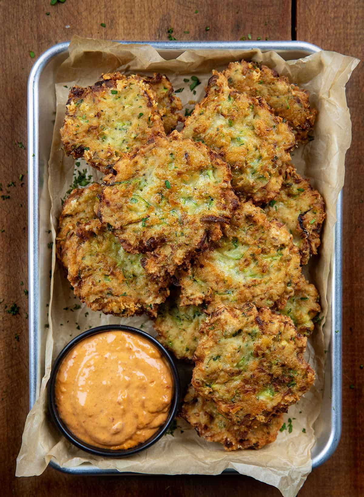 Cheesy Zucchini Chicken Fritters with sauce in a tray on a wooden table from overhead.