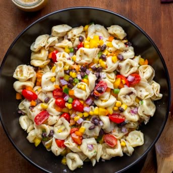 Cowboy Caviar Tortellini Salad in a black bowl on a wooden table from overhead.