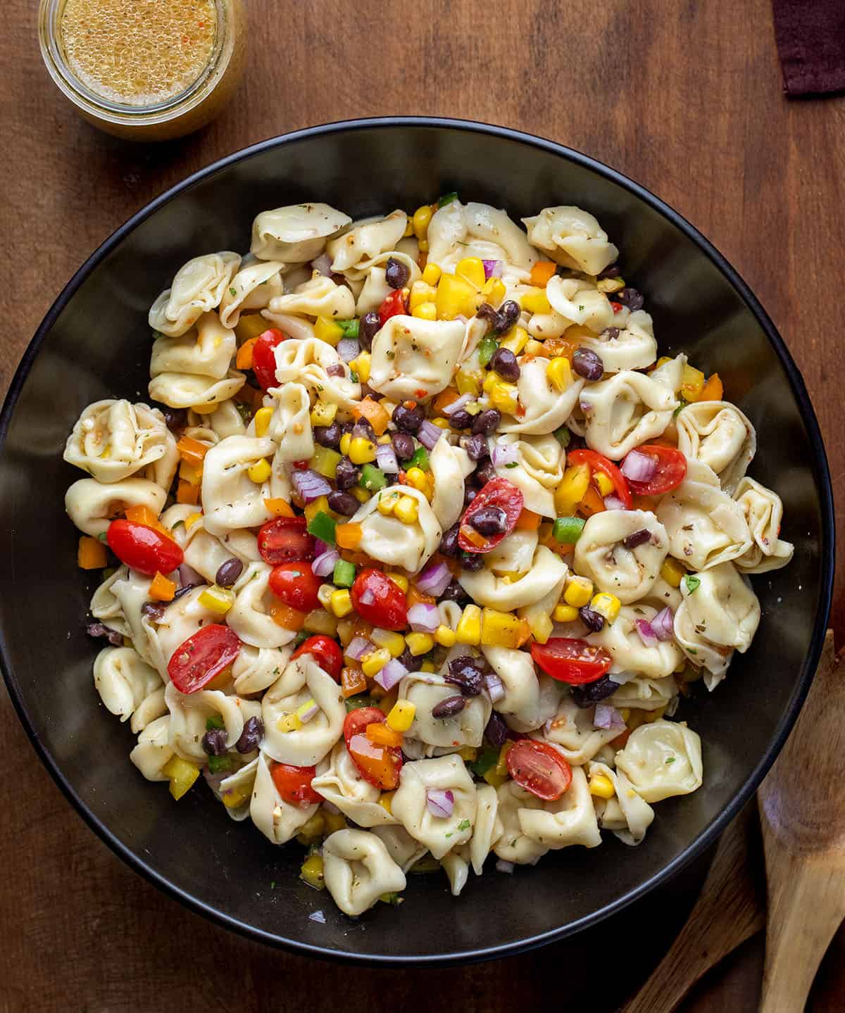 Cowboy Caviar Tortellini Salad in a black bowl on a wooden table from overhead Cowboy Caviar Tortellini Salad in a black bowl on a wooden table from overhead.