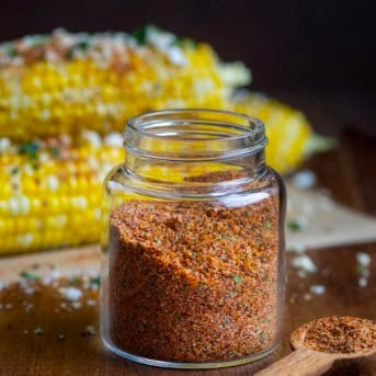 Glass jar of Elote Seasoning Mix in front of esquites corn.