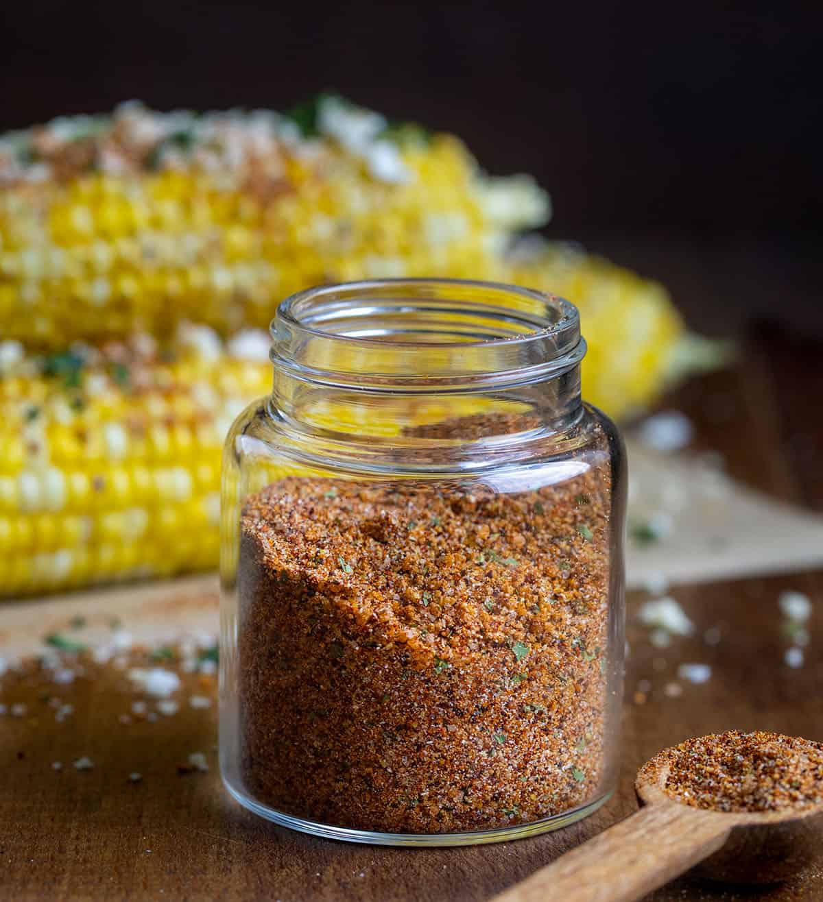 Glass jar of Elote Seasoning Mix in front of esquites corn Glass jar of Elote Seasoning Mix in front of esquites corn.