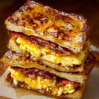 Halved and stacked French Toast Breakfast Sandwich on a wooden table.