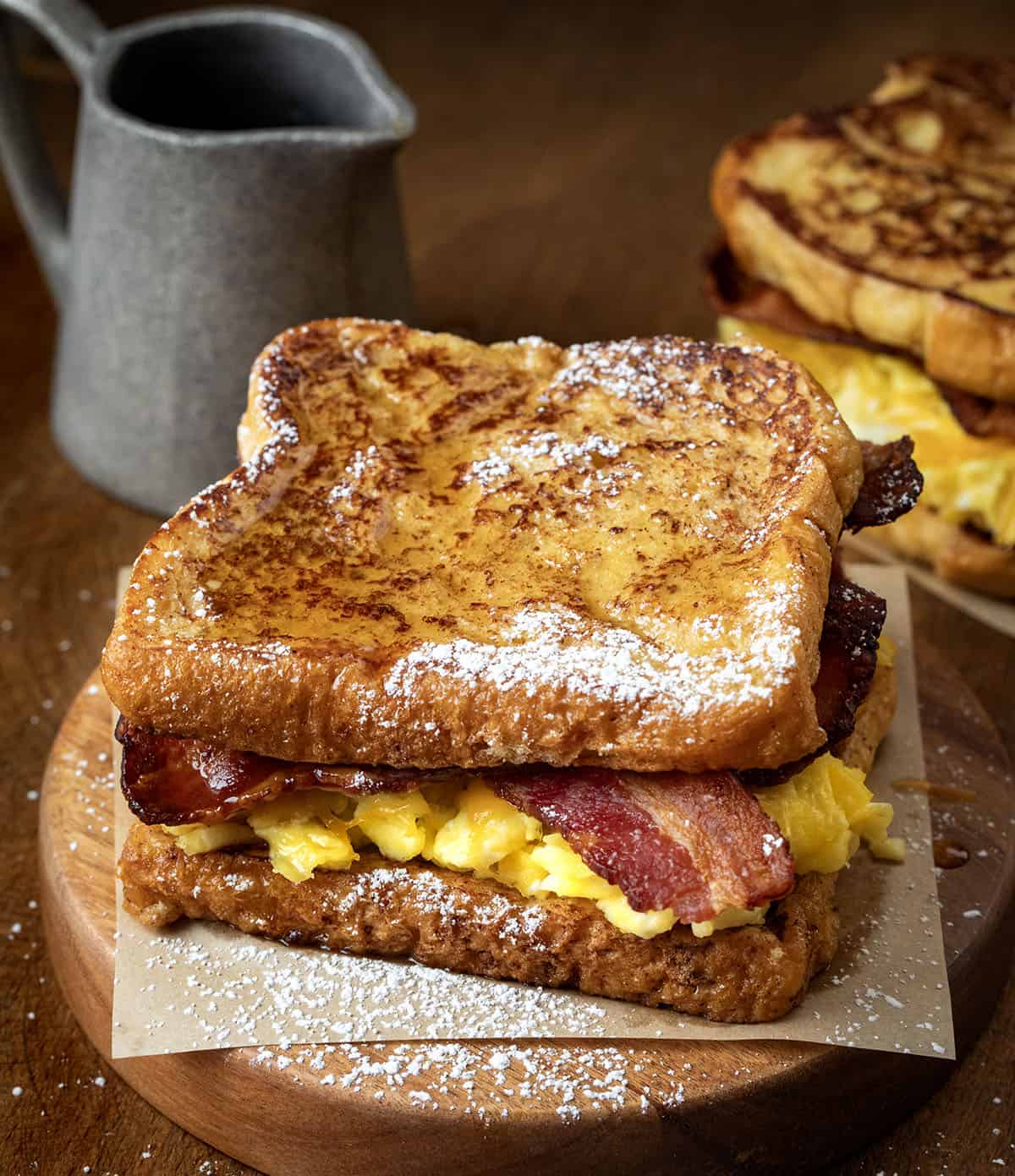 French Toast Breakfast Sandwiches on a wooden table covered in powdered sugar and syrup French Toast Breakfast Sandwiches on a wooden table covered in powdered sugar and syrup.