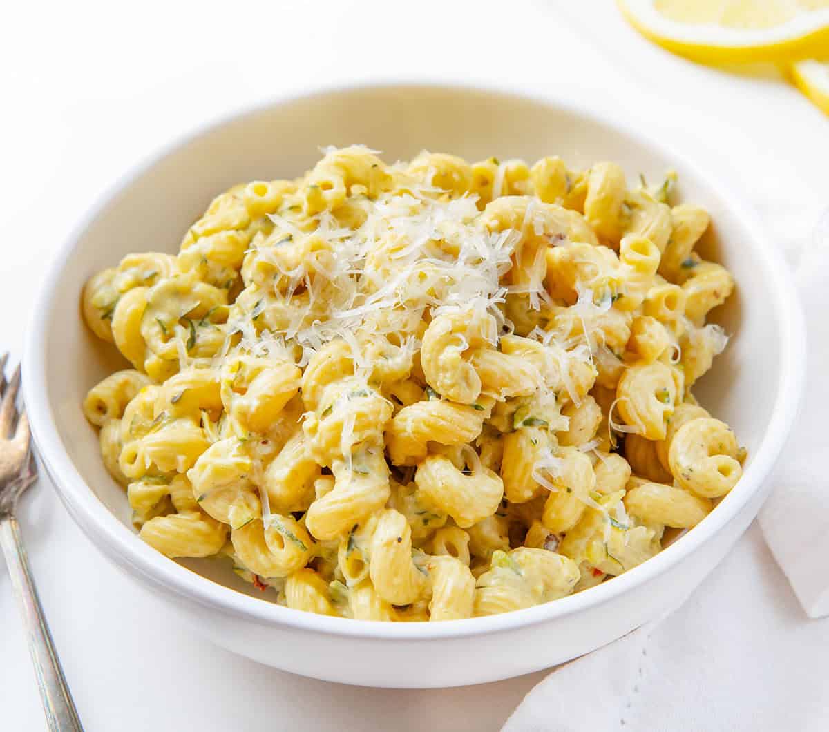 White bowl filled with Garlic Lemon Zucchini Pasta on a white table White bowl filled with Garlic Lemon Zucchini Pasta on a white table.