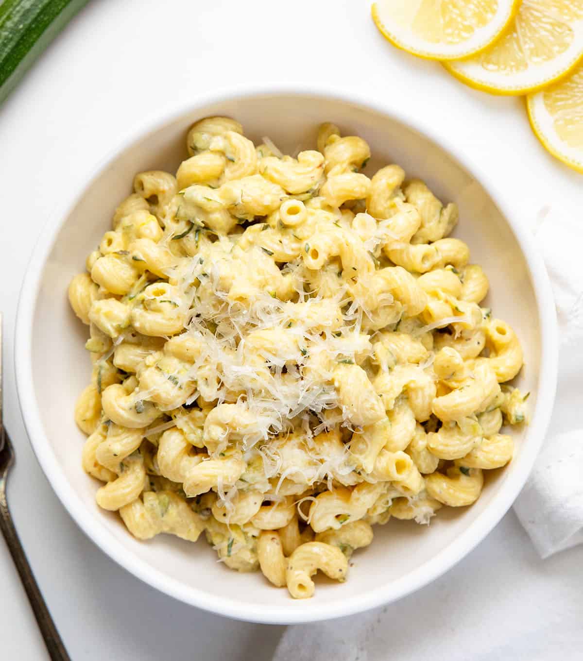 White bowl filled with Garlic Lemon Zucchini Pasta on a white table with lemon slices and zucchini White bowl filled with Garlic Lemon Zucchini Pasta on a white table with lemon slices and zucchini.