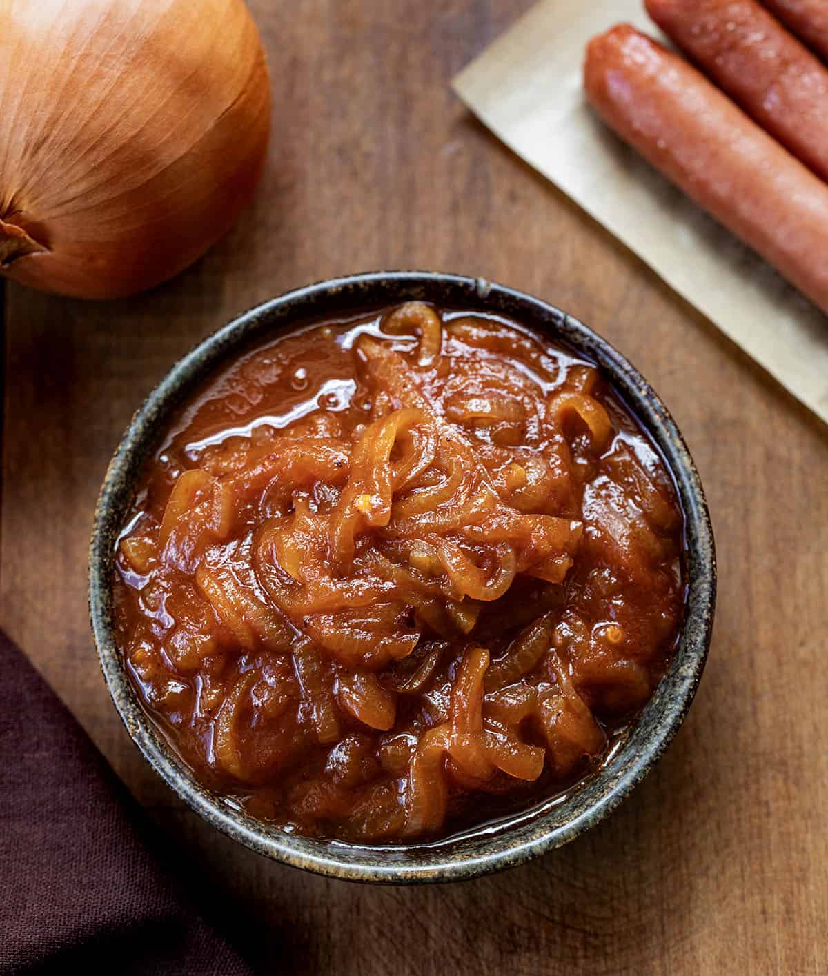 Bowl of Hot Dog Onion Sauce on a wooden table with hotdogs and an onion Bowl of Hot Dog Onion Sauce on a wooden table with hotdogs and an onion.