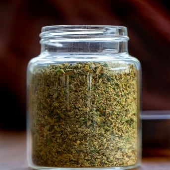 Glass jar of homemade Italian Seasoning on a wooden table.
