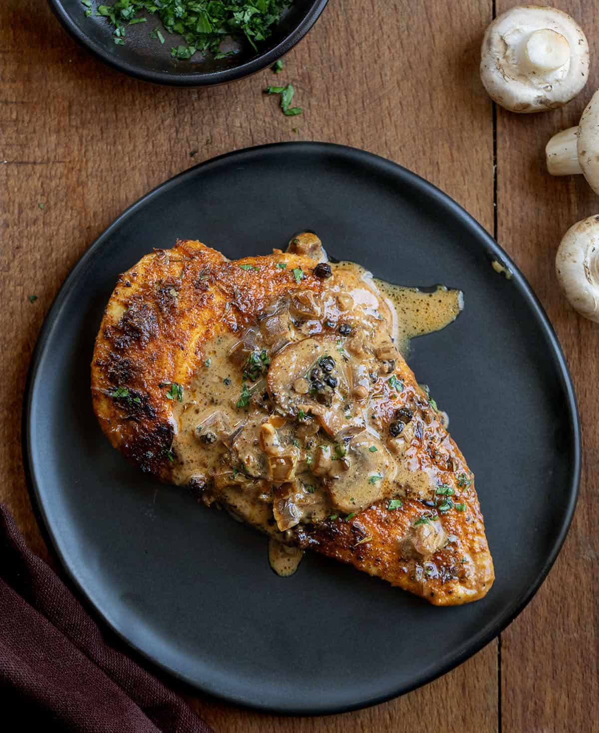 Mushroom Peppercorn Chicken on a black plate on a wooden table from overhead Mushroom Peppercorn Chicken on a black plate on a wooden table from overhead.