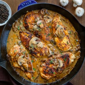 Skillet of Mushroom Peppercorn Chicken on a wooden table with peppercorns and mushrooms.