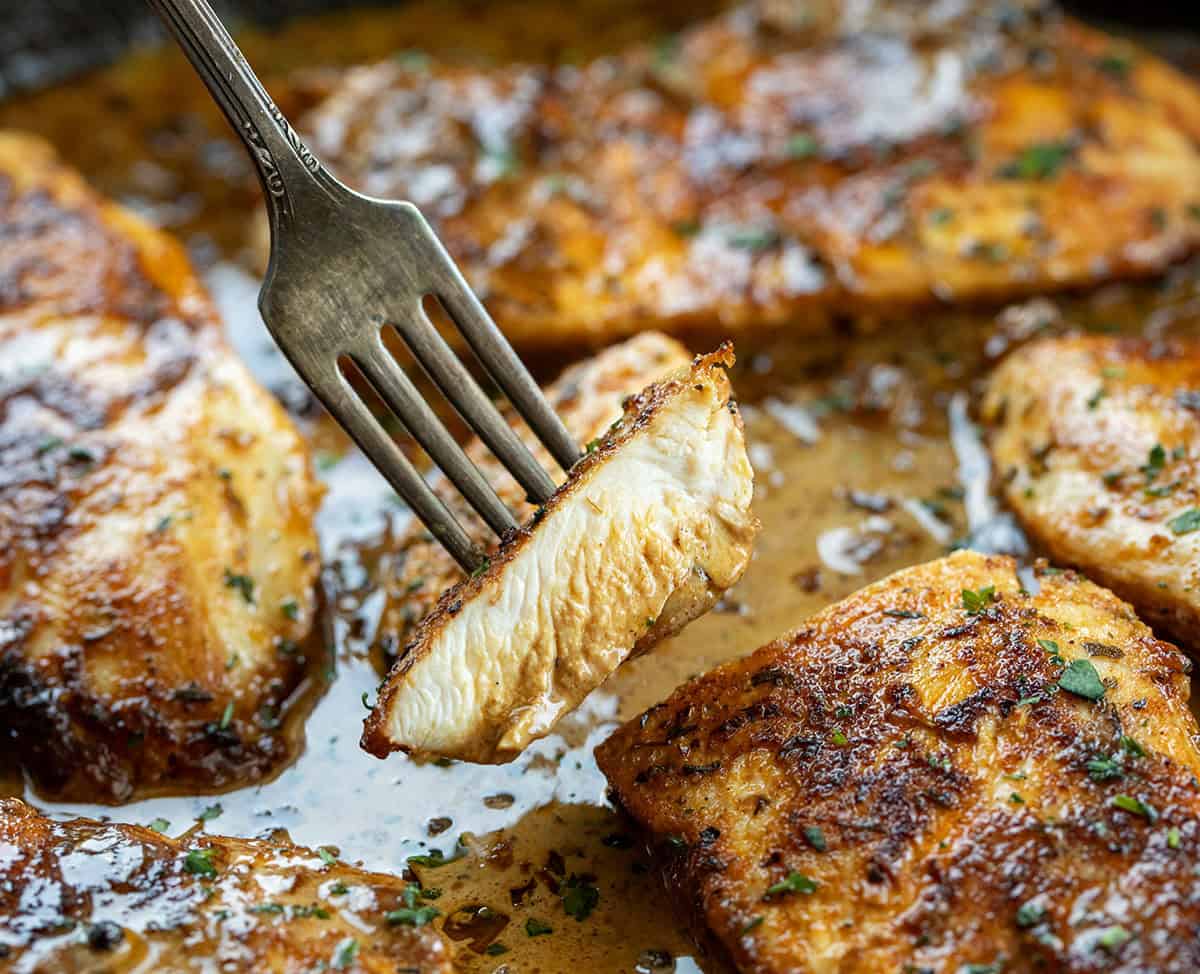 Fork with a piece of Peppercorn Chicken on it being held above the chicken in the skillet Fork with a piece of Peppercorn Chicken on it being held above the chicken in the skillet.