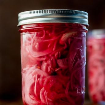 Jars of Pickled Red Onions on a wooden table.
