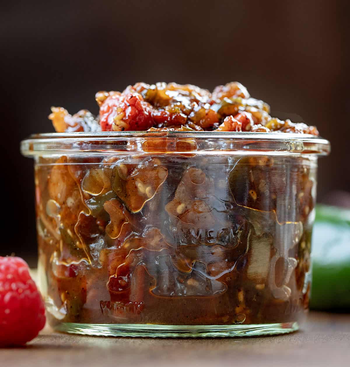 Jar of Raspberry Jalapeño Bacon Jam on a wooden table with fresh raspberry and jalapeno Jar of Raspberry Jalapeño Bacon Jam on a wooden table with fresh raspberry and jalapeno.