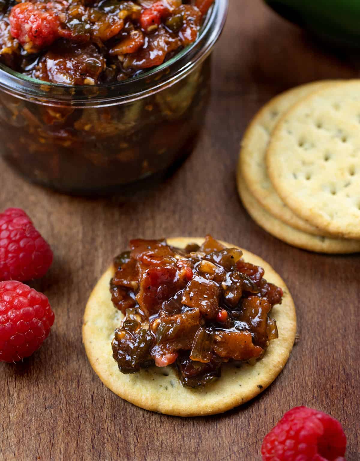 Cracker with Raspberry Jalapeño Bacon Jam on it near the jar Cracker with Raspberry Jalapeño Bacon Jam on it near the jar.