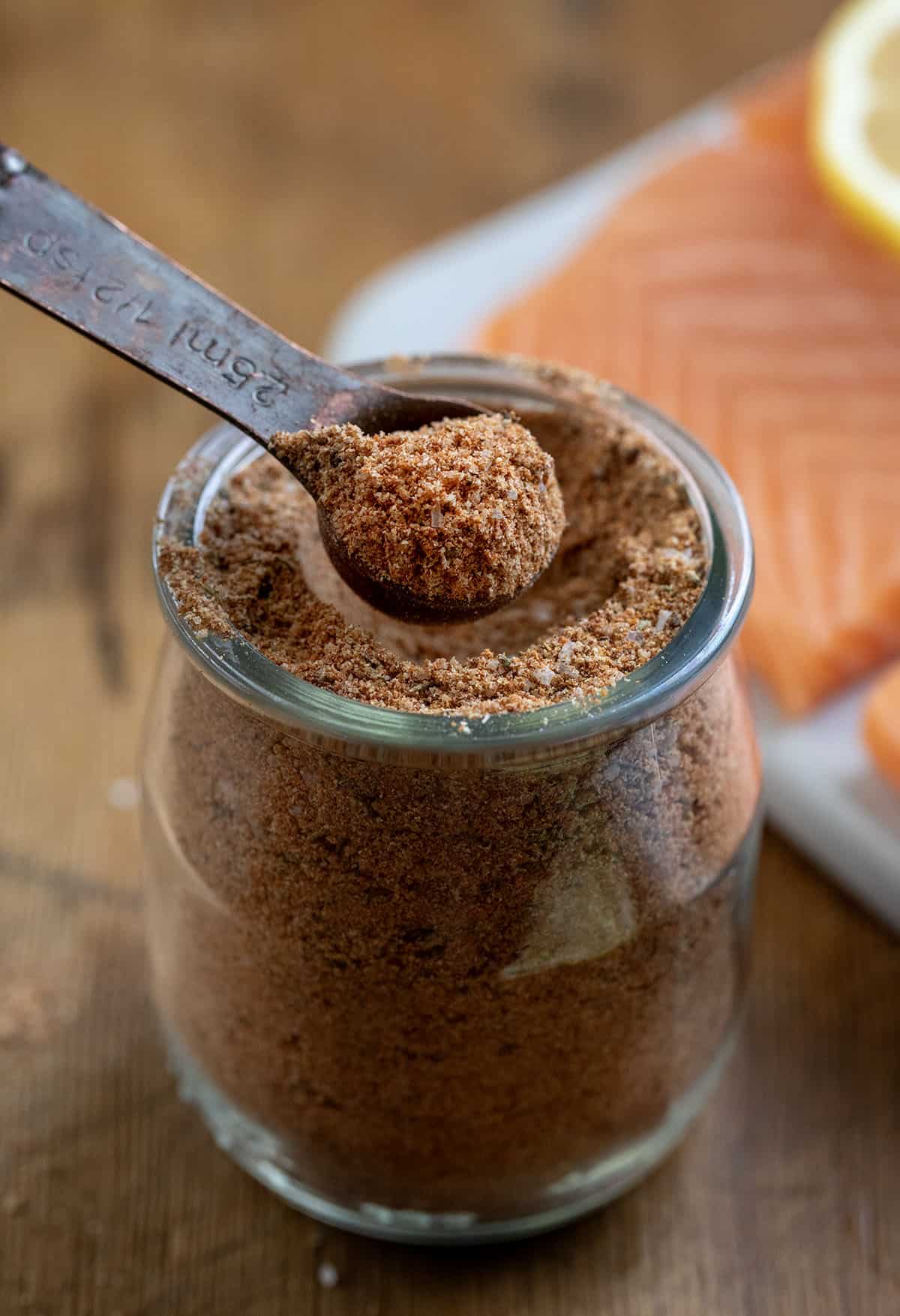 Measuring spoon in a jar of Salmon Seasoning next to some fresh salmon Measuring spoon in a jar of Salmon Seasoning next to some fresh salmon.