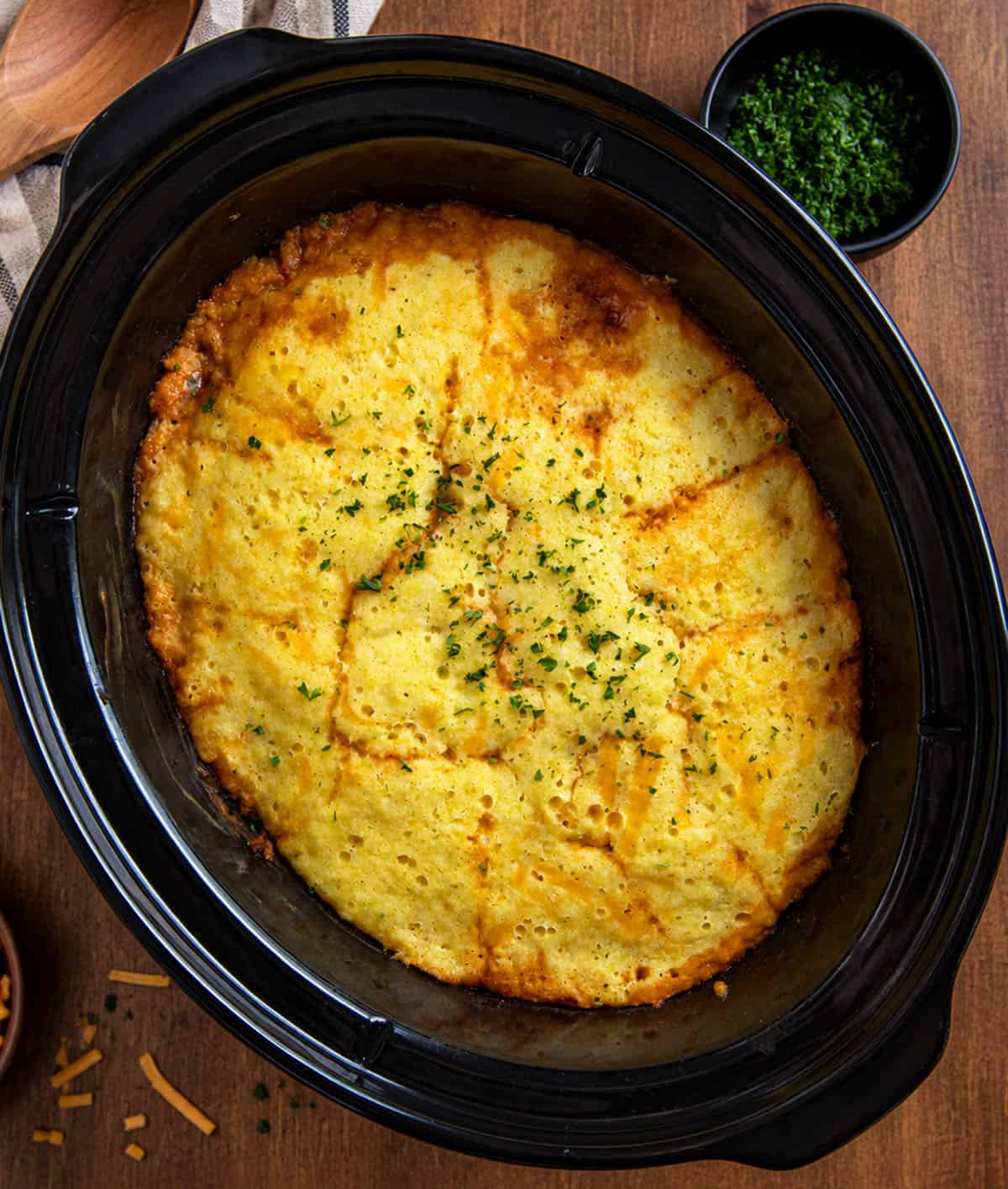 Slow Cooker Cornbread Cowboy Casserole on a wooden table from overhead Slow Cooker Cornbread Cowboy Casserole on a wooden table from overhead.